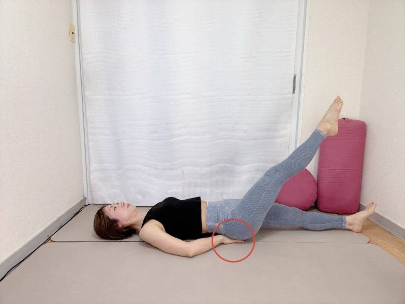 両手をお尻の下に敷いて左脚を斜め上に伸ばした仰向けの体勢