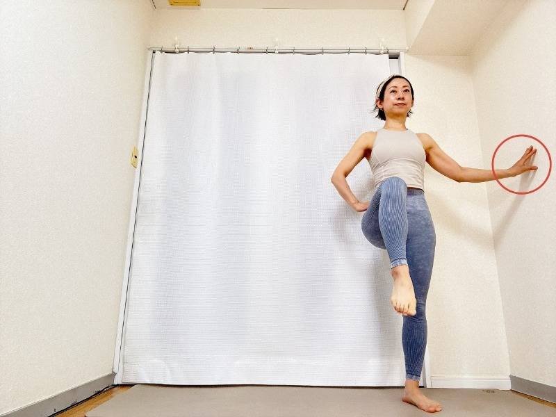 壁に手をついて立ち、片膝を曲げて腿上げをする腸腰筋を鍛えるエクササイズ