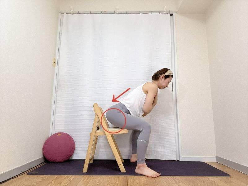 両手を胸の前でクロスして椅子の前で立ち、背筋を伸ばしたままお尻をうしろに引いて、椅子に軽く座るスクワット