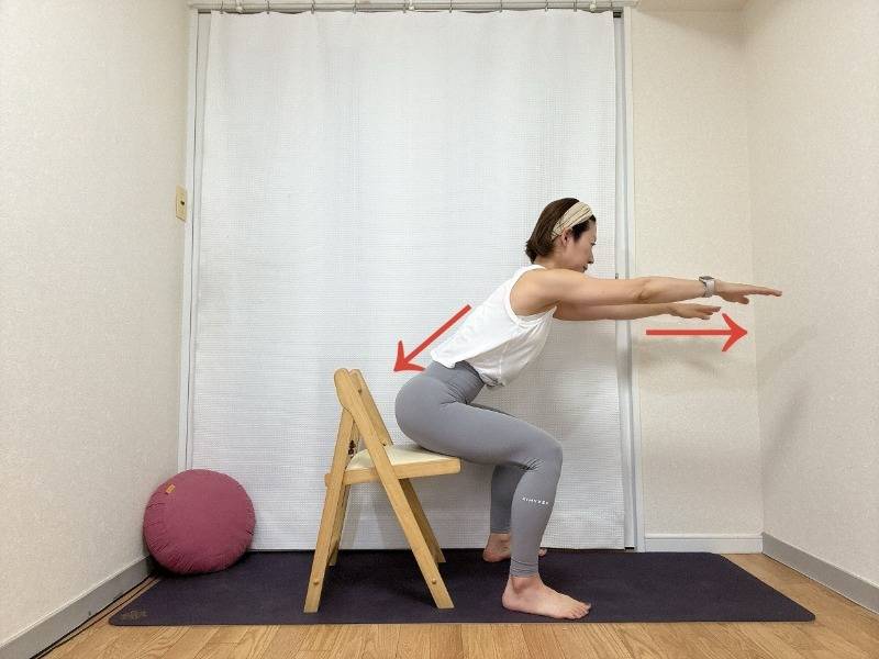 両手を肩の高さで前に伸ばし、後ろの椅子に軽く腰を下ろすスクワットエクササイズ