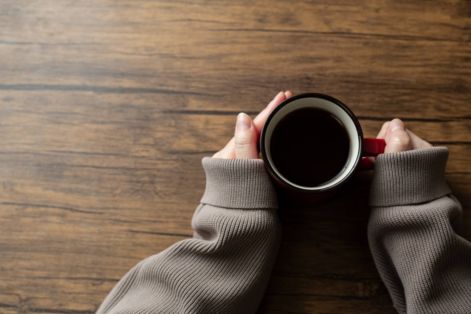 ホットコーヒーを両手で持つ女性の手元