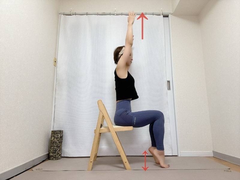 椅子に座り、両手を頭上に伸ばしてかかとを上げ下げするむくみ解消エクササイズ