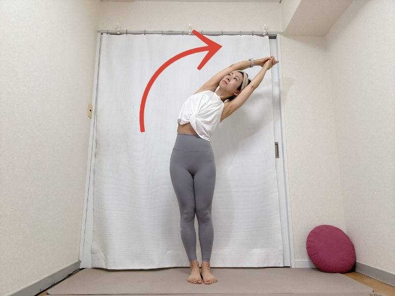 人差し指を伸ばして両手をを組んで頭上に伸ばして立ち、上体を右に倒した月のポーズ