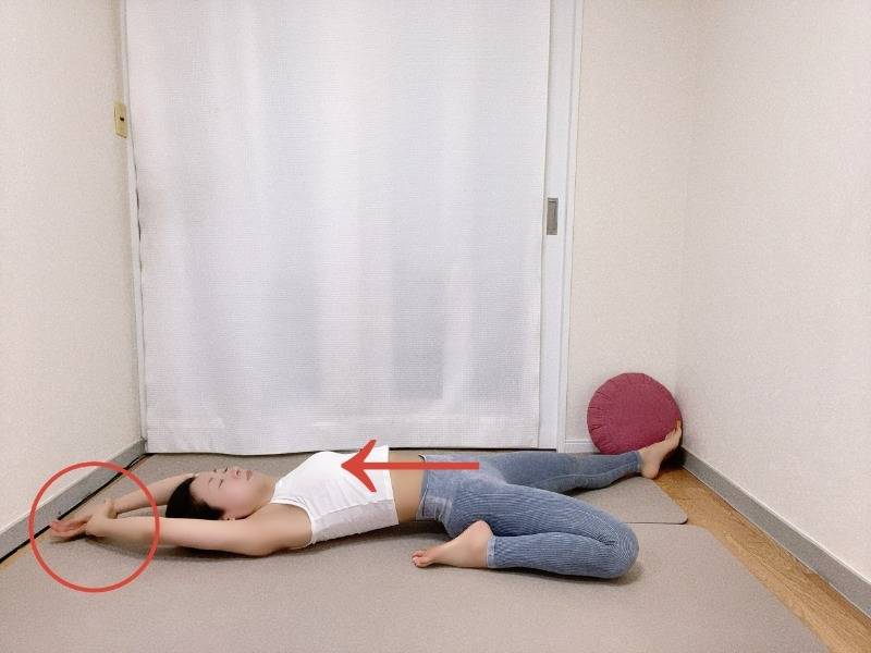 左膝を曲げた半分の割座から仰向けになり両手を頭上に伸ばし、右手で左手首をつかんだ体勢、