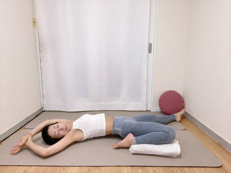左膝を曲げた半分の割座から仰向けになり、膝下にタオルを挟み、膝の負担を軽減して行うストレッチ