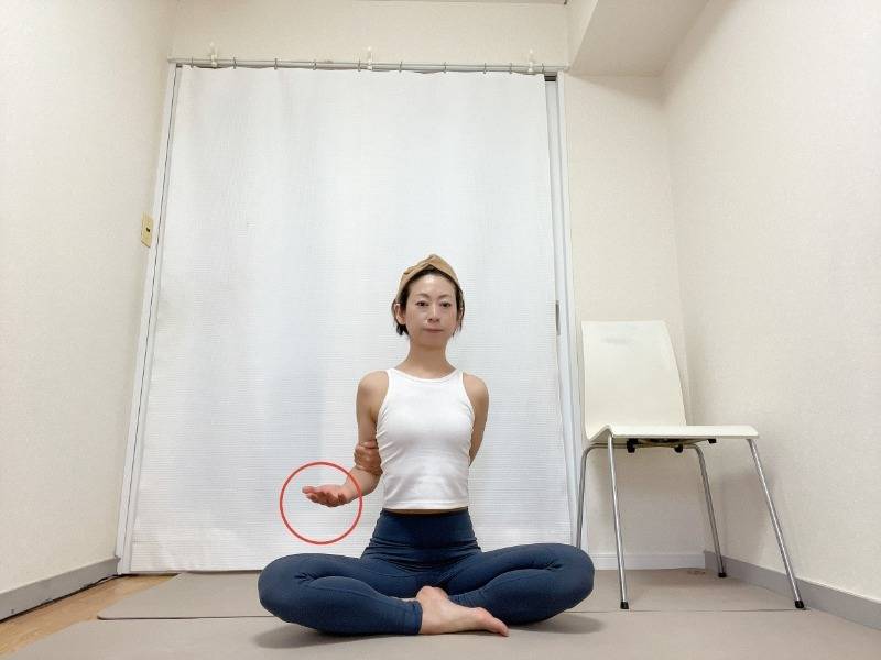 手のひらを上に向けて左肘を曲げ、右手を背中に回して左肘を掴んだあぐらの姿勢