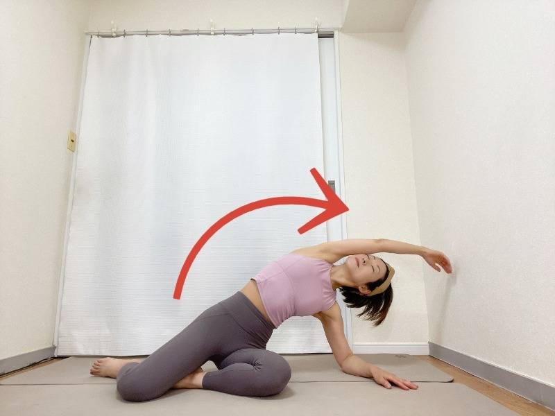 右脚を前にした横座りから、右肘を床につき、左手を引き上げて上体を右に倒す左体側を伸ばすストレッチ