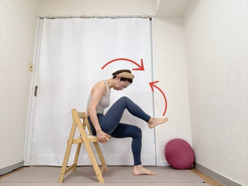 椅子に座り、上体を前にかがめながら左膝を胸に寄せた体勢