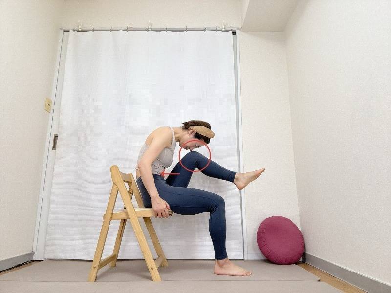 椅子に座り、上体を前にかがめ、左膝と鼻先を寄せた体勢