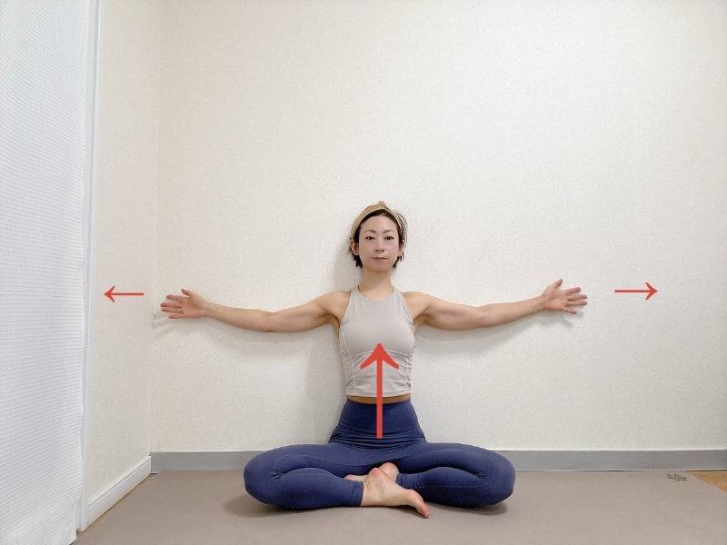 壁を背にしてあぐらで座り、両手を肩の高さに開いた体勢