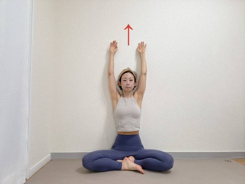 壁を背にしてあぐらで座り、両手をバンザイした体勢