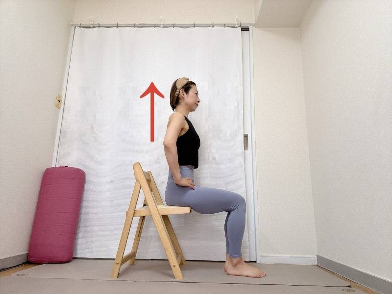 手を腰に添え、椅子に浅く座った体勢