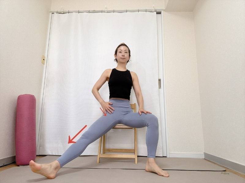 椅子に座って左脚を軽く開いた半分の開脚から脚の付け根を手でさすってほぐすセルフマッサージ