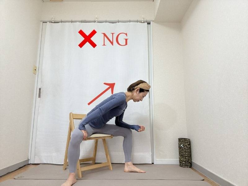 脚を大きく開いて椅子に座り、右肘を腿に乗せ、背中を伸ばして行うNGストレッチ