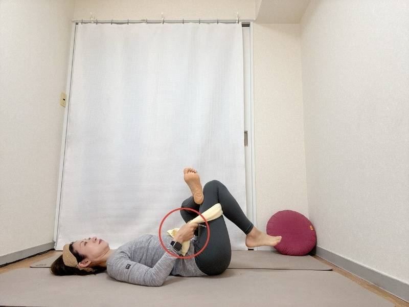 仰向けで軸足の腿裏にタオルを通して胸に寄せた針の糸通しのポーズ