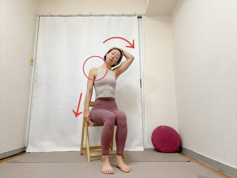 椅子に座り、左腕を体側に、頭を右に傾けて右手をこめかみに添えた首のストレッチ