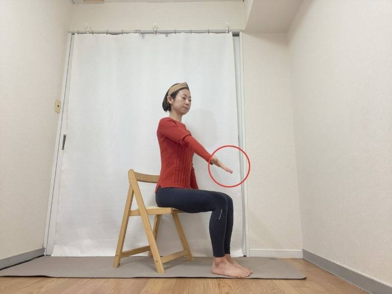 左手の平を天井に向けて体の前に伸ばし、右手を体側に下して椅子に座った体勢