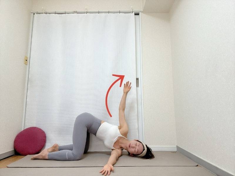 四つ這いで左脇の下に右腕を通し、左手を天井に引き上げたキャットストツイストポーズ