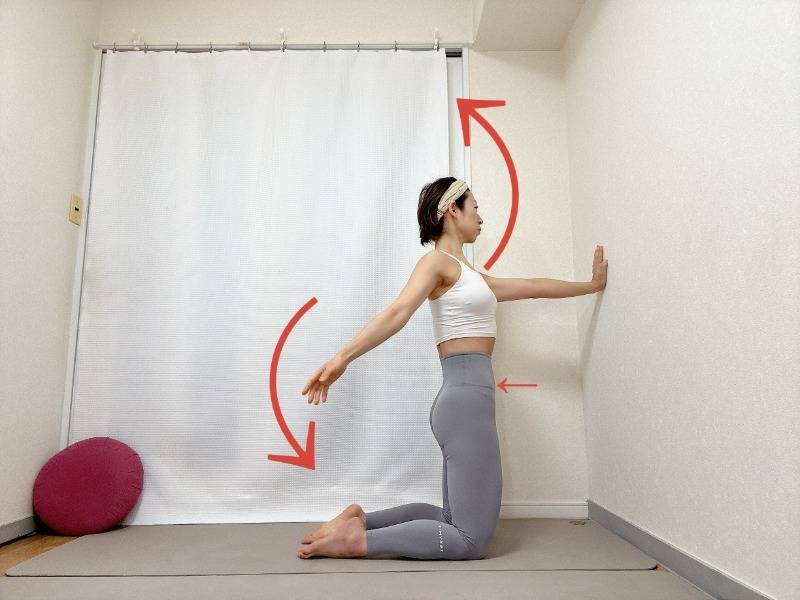 壁に向かって膝立ちになり、片手を壁に、もう片方の腕を大きく回す肩こり解消エクササイズ