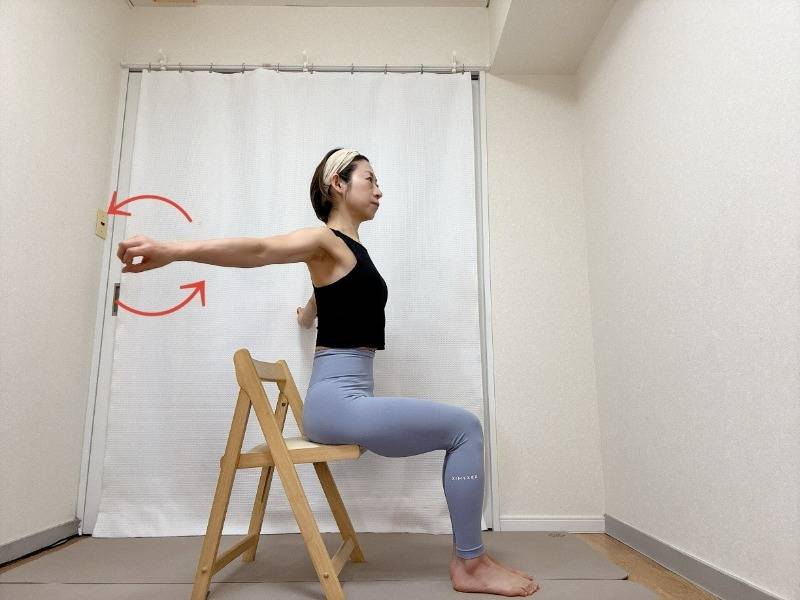 両手を肩の高さで開いて椅子に座り、手の甲を前に向けて軽く握って腕をうしろに回すエクササイズ