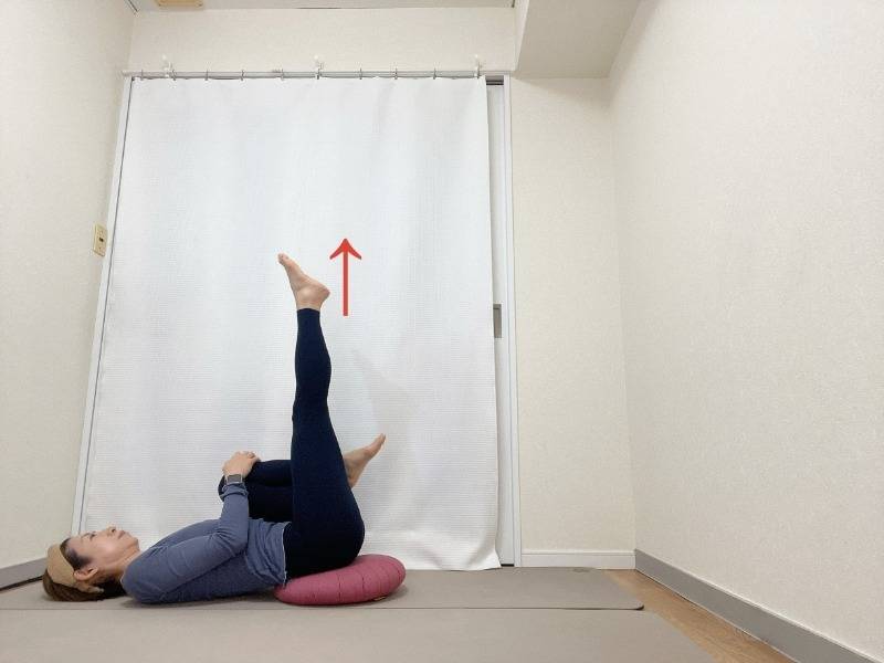お尻の下にクッションを敷いて膝を抱えた仰向けから左脚を天井に伸ばした体勢