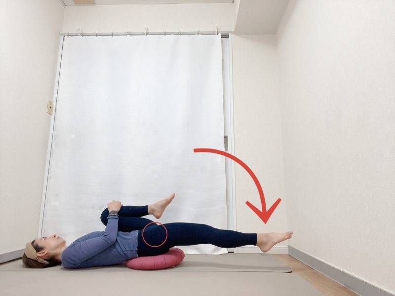 お尻の下にクッションを敷いた仰向けから右膝を抱え、左脚を伸ばした腸腰筋のストレッチ