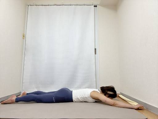 タオルの端を持ち、両手を頭の上に伸ばしたうつ伏せの体勢