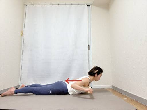 タオルの端を持ち、両手を頭の上に伸ばしたうつ伏せかわ、肘を曲げて胸に引き寄せた背中のエクササイズ