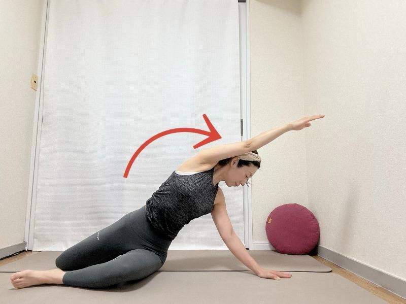 膝を立てて座っり、右手を後ろの床に着いて左手を引き上げ、両膝を右に倒して後ろを振り返って左腰から体側を伸ばすストレッチ