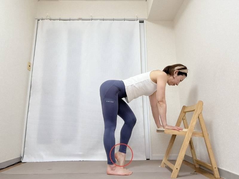 椅子の座面に手をつき、背筋を伸ばして前傾。右のかかとを上げて深く膝を曲げ、左脚の裏側全体を伸ばした体勢