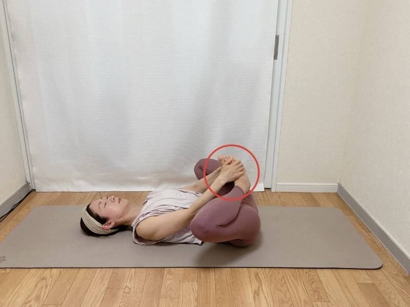 仰向けで両膝を抱え、膝を外に開いて両手でつま先を抱えた体勢
