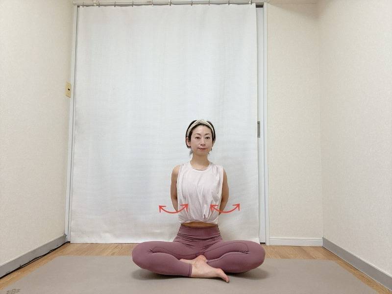 あぐらで座り、肘を曲げて軽く握った手を腰に添え、肘を後ろに引いて肩甲骨を寄せた体勢