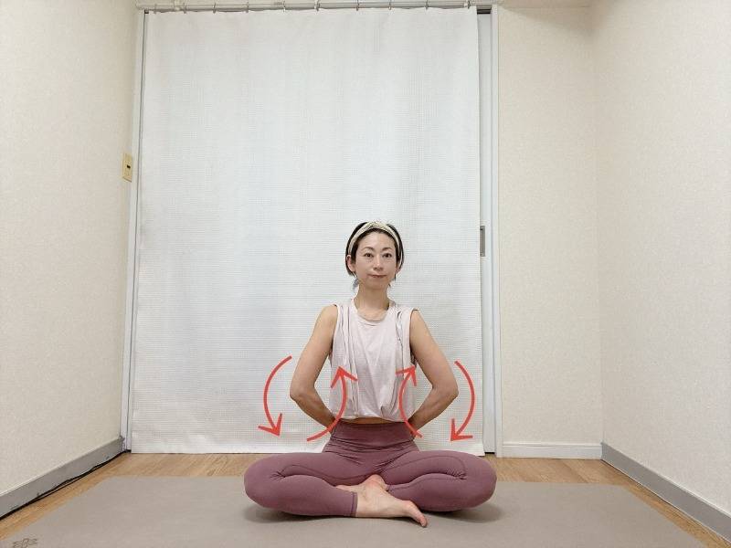 あぐらで座り、肘を曲げて軽く握った手を腰に添え、肩甲骨から腕を動かして前後に回す肩甲骨はがしエクササイズ