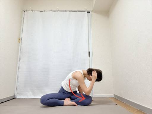 左手を後頭部に添えたあぐらで座り、背骨を丸め名がrあ左肘を右膝に寄せるツイストエクササイズ