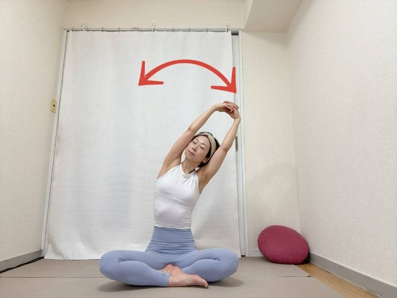 あぐらで座り、両手を組んで頭上に引き上げて左右にしならせる背骨のストレッチ