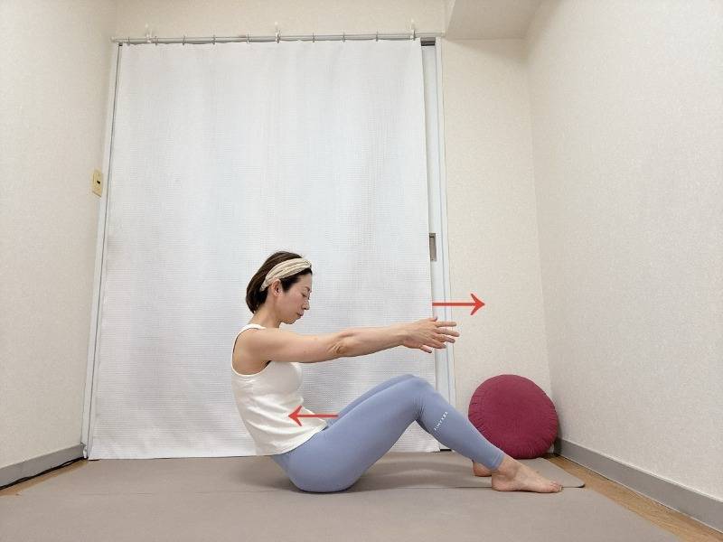 両膝を立てて座り、両手を体の前に伸ばし、お腹を引き込みながら背骨を丸めるエクササイズ