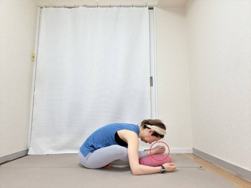 左かかとを少し前に出し、クッションの上に乗せたあぐらから上体を前に傾けるお尻のストレッチ