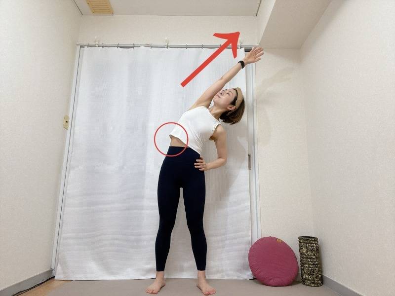 足を腰幅～肩幅程度に開き、左手を斜め右上に伸ばして左体側を伸ばして立った体勢