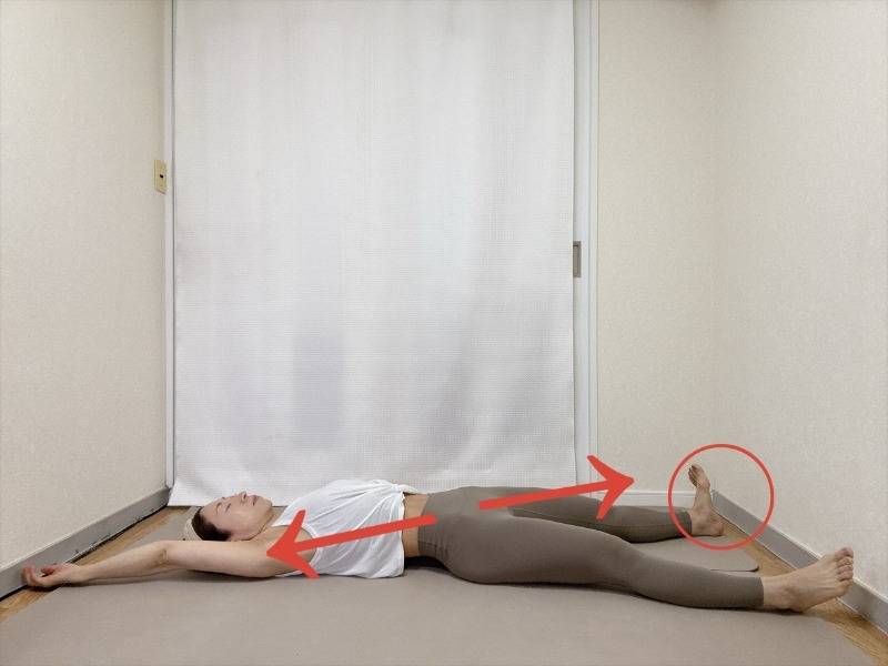 仰向けで左手を斜め上に、右かかとをつきだして対角線状に体を伸ばすストレッチ