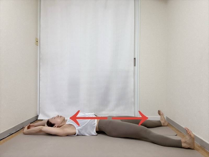 仰向けで両手を頭の腕で組み、かかとを突き出して全身を伸ばすストレッチ