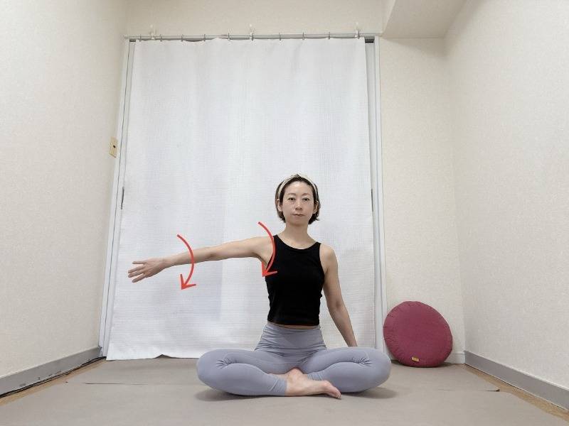 あぐらで座り、横に伸ばした左腕を内側にねじるストレッチ