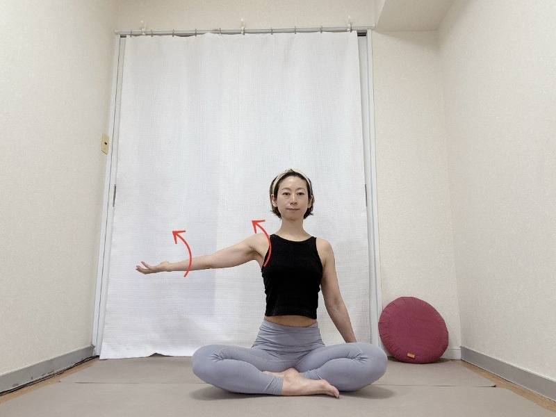 あぐらで座り、横に伸ばした左腕を外側にねじるストレッチ