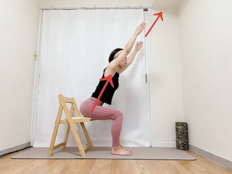 椅子に座り、背筋を伸ばしたまま上体を前に傾け、両腕を斜め上に伸ばした体勢