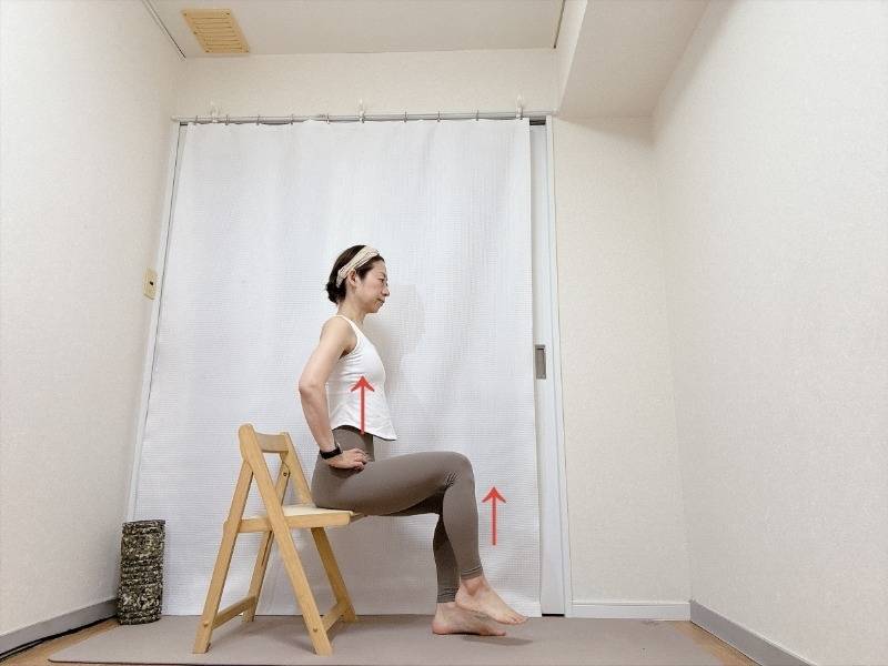 両手を腰に添え、背筋を伸ばして椅子に座り、片脚を床から少し浮かせた体勢