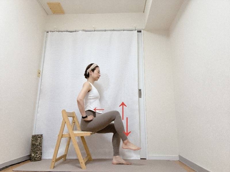 両手を腰に添え、背筋を伸ばして椅子に座り、片脚を床から少し浮かせて上下に動かすトレーニング
