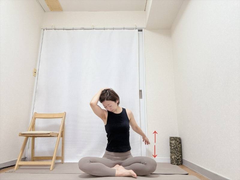 あぐらで座り、左手を後頭部に添えて頭を左下に傾け、後ろに引いた右腕を上下に動かす肩まわりのストレッチ。
