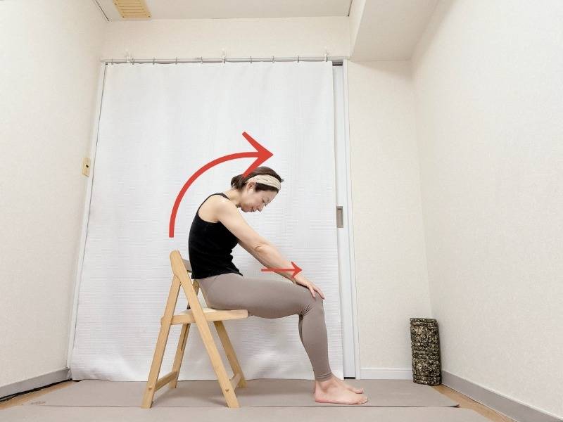 両手を膝の方に滑らせて背中を丸める、椅子に座って行うキャットポーズストレッチ