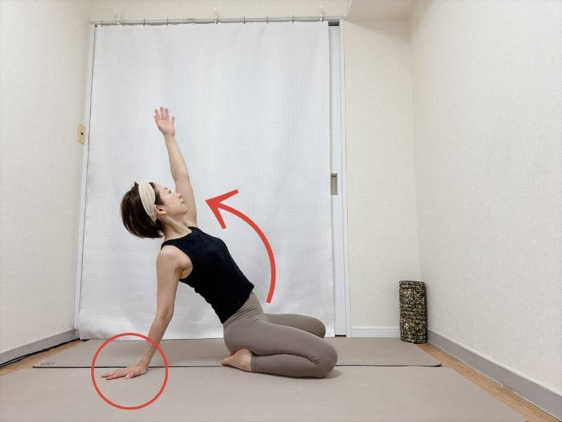 正座から左手を後ろの床に着き、右手を斜め上に伸ばして胸を開くラクダのポーズ
