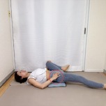 お尻の下にブランケットを敷いた仰向けから左脚の付け根に手を添えて膝を伸ばし、右膝を胸に寄せて外に開いた内転筋のストレッチ
