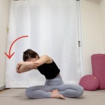 あぐらで座り体の前で両肘を抱え、背骨を丸めながら肘を左に引いた体勢